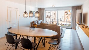 Ett modernt vardagsrum med ett runt matbord, svarta stolar, en soffa och en tv.
