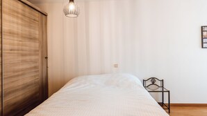 Ett sovrum med en säng, en garderob i trä, en hängande lampa och ett litet sängbord.