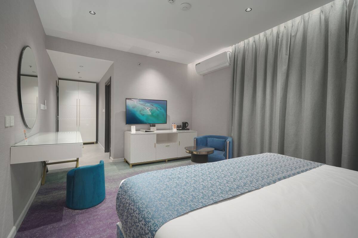A modern hotel room with a bed, a desk, a chair, a TV, and a wardrobe.