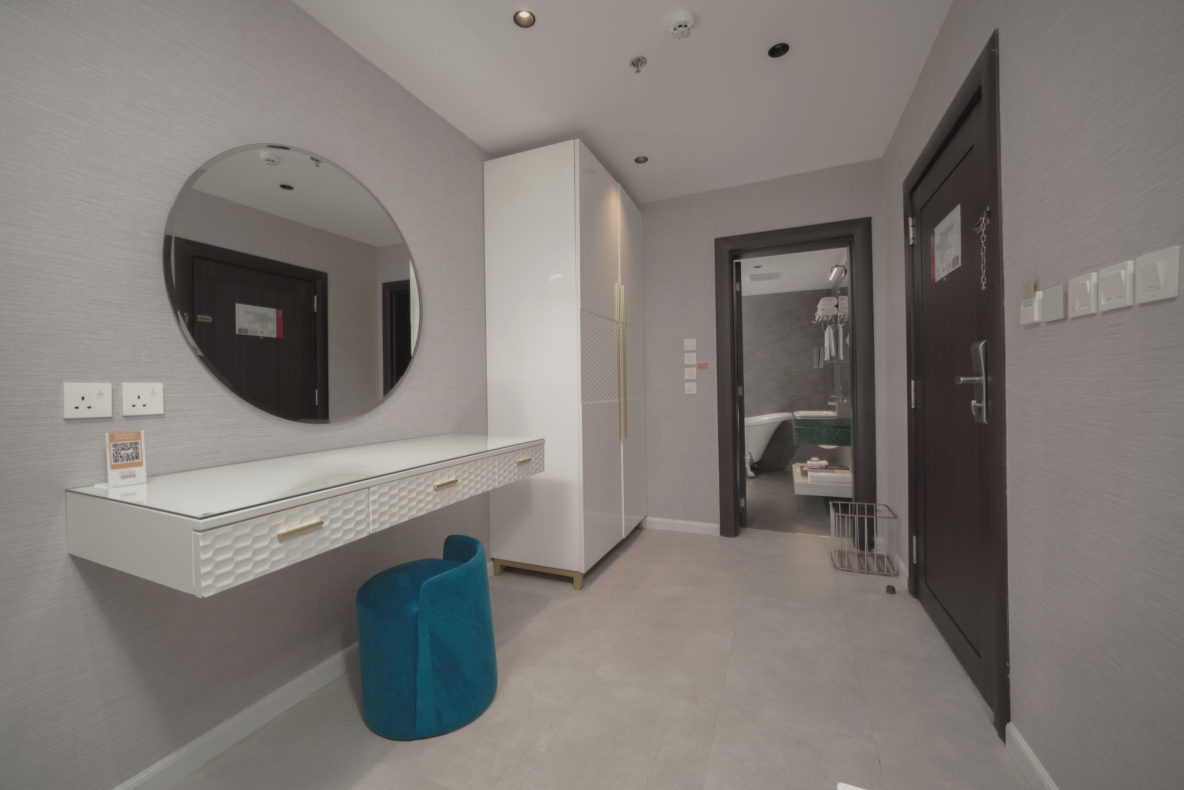 A modern bathroom with a white vanity, a round mirror, and a blue trash bin.
