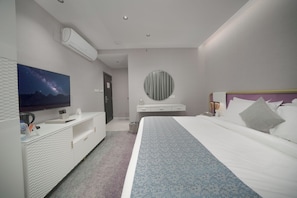 Una habitación de hotel moderna con cama, televisión, espejo redondo y cómoda blanca.