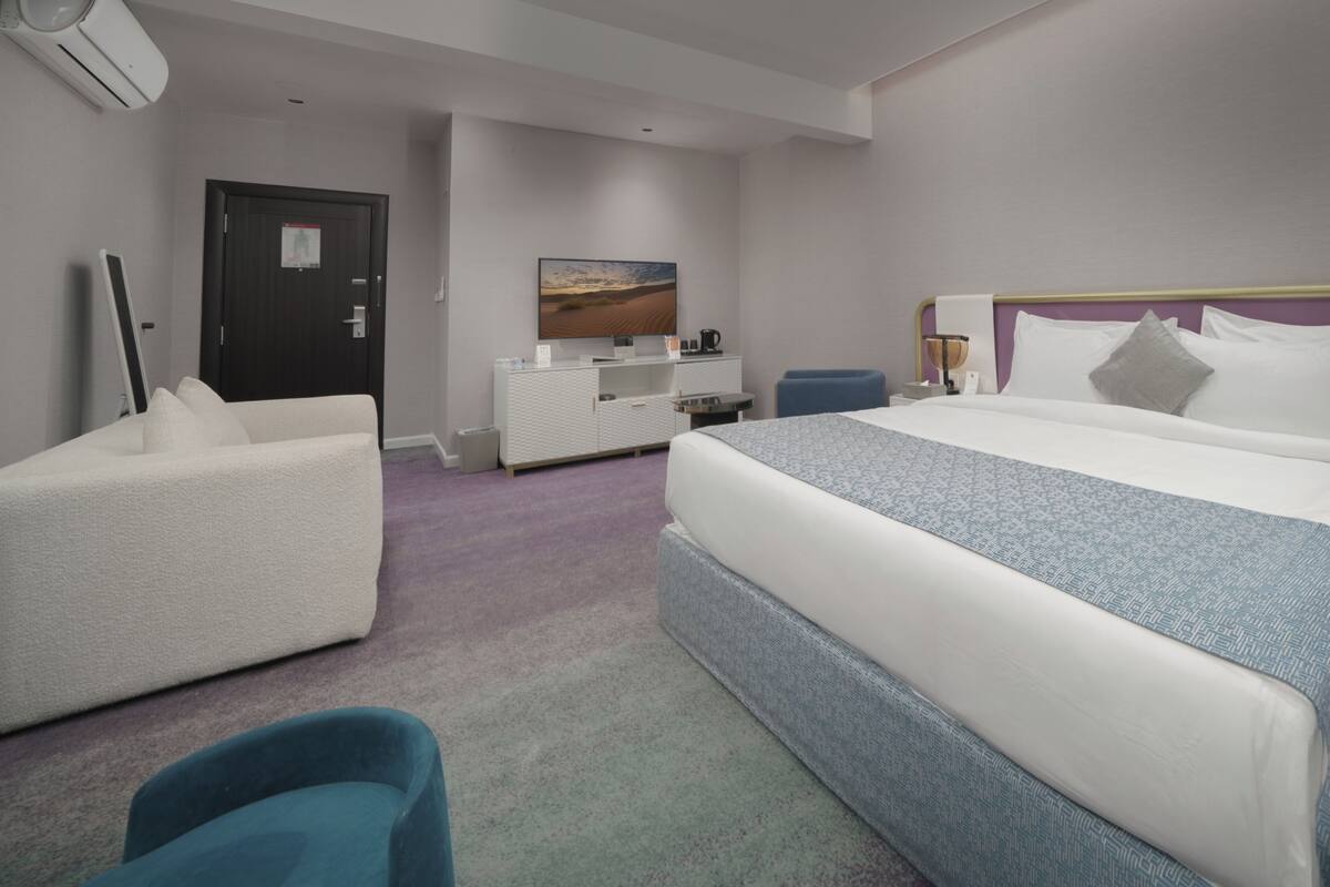 A hotel room with a bed, a white sofa, a small table, a TV, and a door.