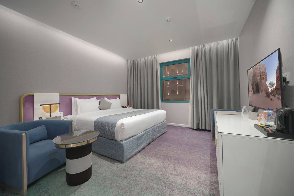 A hotel room with a bed, a desk, a chair, a TV, and a window with curtains.