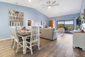 A dining area with a table and chairs, a sofa, a ceiling fan, and a view through a glass door.