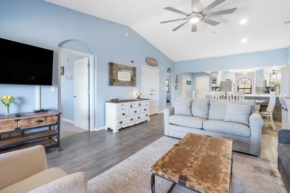 A spacious living room with a sofa, coffee table, and TV. There is a kitchen area in the background.