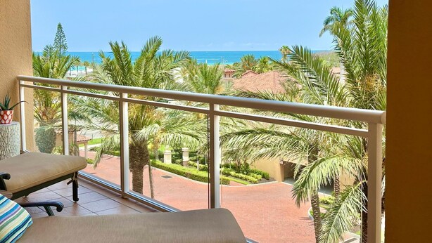 A balcony with a view of the beach, palm trees, and a clear blue sky. - Belle Harbor 506W Panoramic Views (Clearwater Beach)