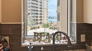 A bathroom with a window view of a high-rise building and a beach. - Belle Harbor 506W Panoramic Views (Clearwater Beach)