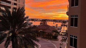 A sunset view from a high-rise building overlooking a marina with boats, palm trees, and a small building with a red-tiled roof. - Belle Harbor 506W Panoramic Views (Clearwater Beach)