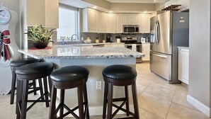 A modern kitchen with a central island, stainless steel appliances, and a large window. - Belle Harbor 506W Panoramic Views (Clearwater Beach)