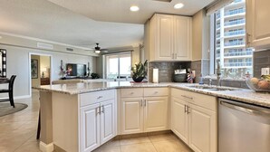 A spacious kitchen with white cabinetry, a large island, and a view of a residential building. - Belle Harbor 506W Panoramic Views (Clearwater Beach)
