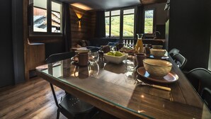 Un comedor moderno con una mesa de cristal, suelo de madera y ventanas grandes que ofrecen vistas al exterior.