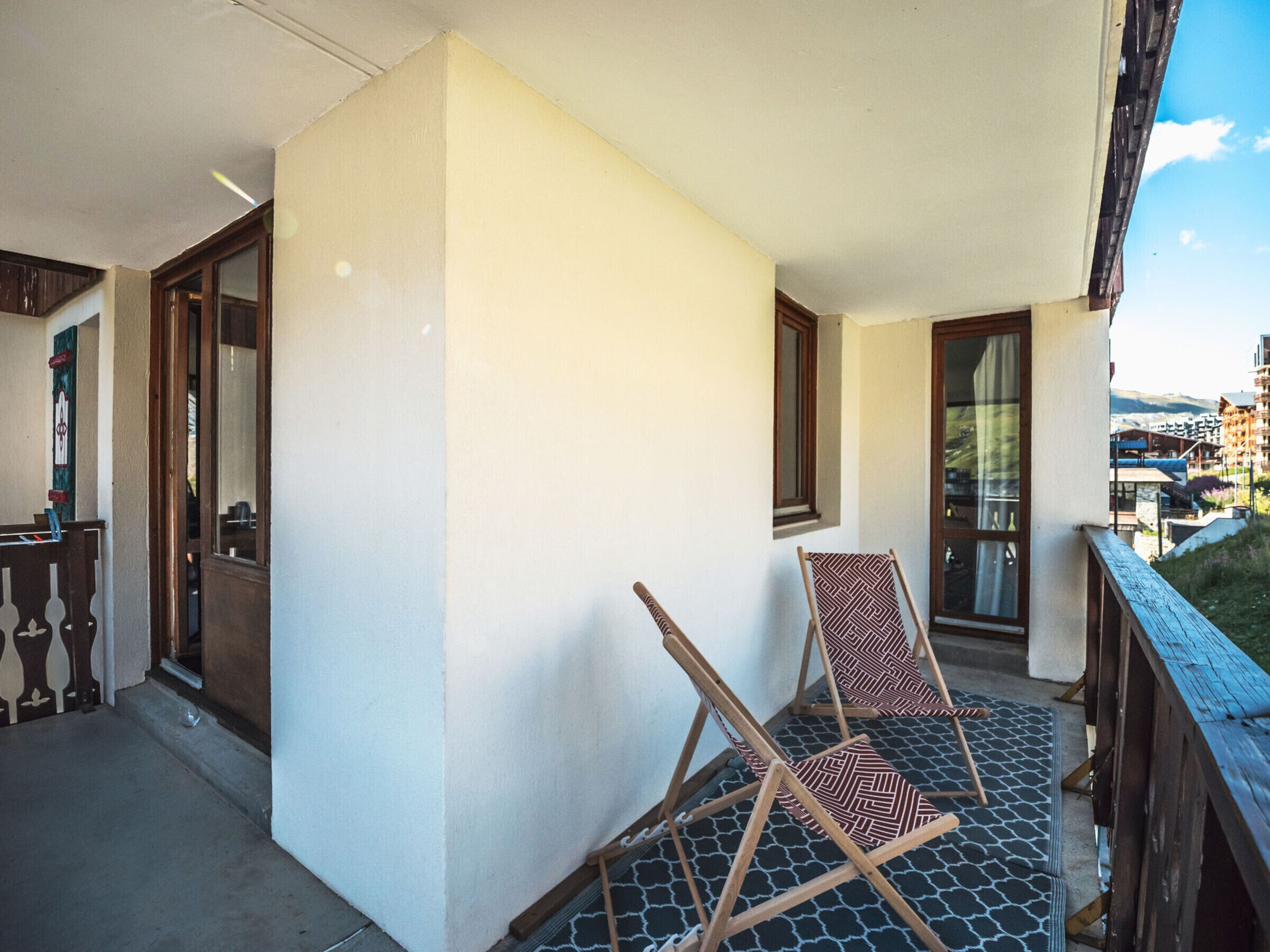 A balcony with a wooden railing, a folding chair, and a patterned rug.