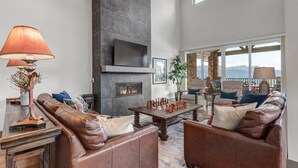 A spacious living room with a fireplace, leather sofas, a coffee table, and a large window offering a view of the mountains.