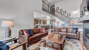A spacious living area with a brown leather sofa, a wooden coffee table, and a staircase leading to an upper level.