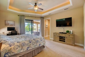Un dormitorio con una cama grande, un ventilador de techo, un televisor y vistas al exterior.