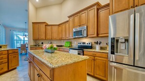 A kitchen with wooden cabinets, granite countertops, stainless steel appliances, and a central island with flowers. - Villa SunnySide- perfect for families and boaters (Cape Coral)