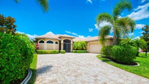A residential property with a paved driveway, a garage, and well-maintained landscaping including palm trees and shrubs. - Villa SunnySide- perfect for families and boaters (Cape Coral)
