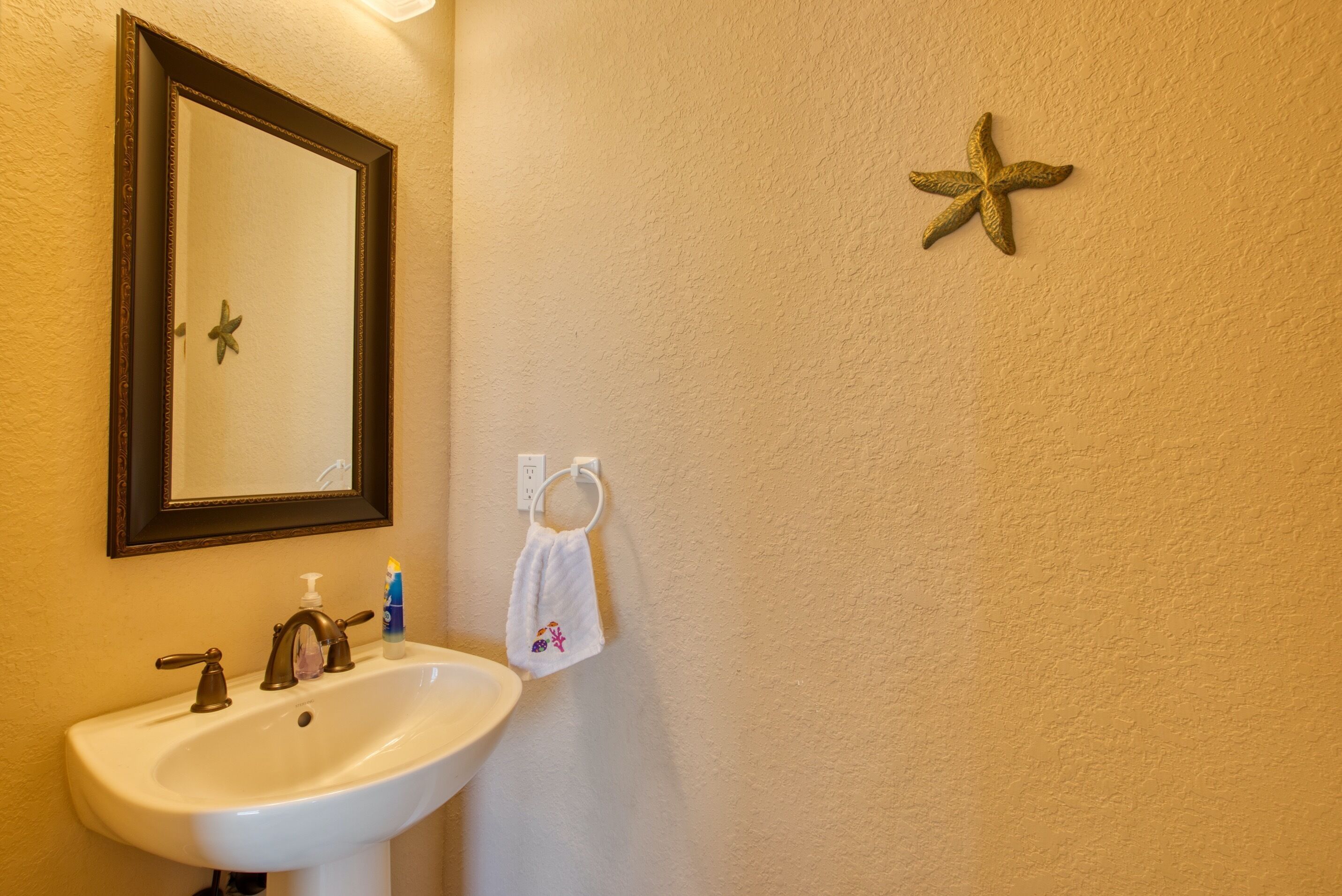 A bathroom with a white sink, a mirror with a starfish decoration, and a towel hanging on the wall.
