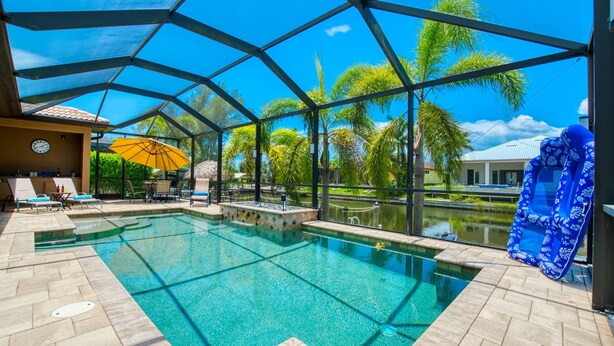 A pool area with clear blue water, surrounded by palm trees and a covered structure. - Villa SunnySide- perfect for families and boaters (Cape Coral)