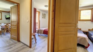 A room with a wooden door, a bed, a small table, and a chair. - Spacious apartment in Les Menuires, 3 rooms, at the foot of the slopes (Les Menuires)