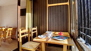 A wooden dining table with chairs, a window with a metal railing, and a door leading to another room.