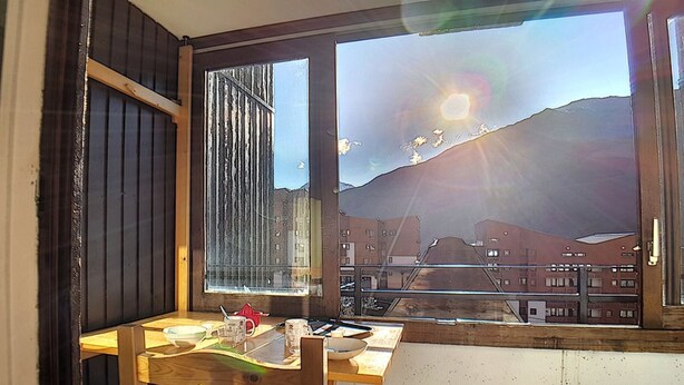 A room with a wooden table and chair, a window with a view of buildings and a mountain, and a door with a wooden frame.