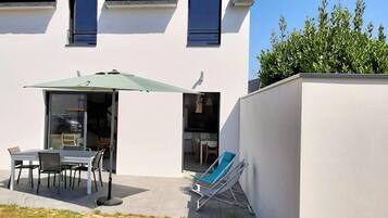 Une terrasse extérieure avec une table et des chaises, un parasol vert et un fauteuil de jardin bleu.