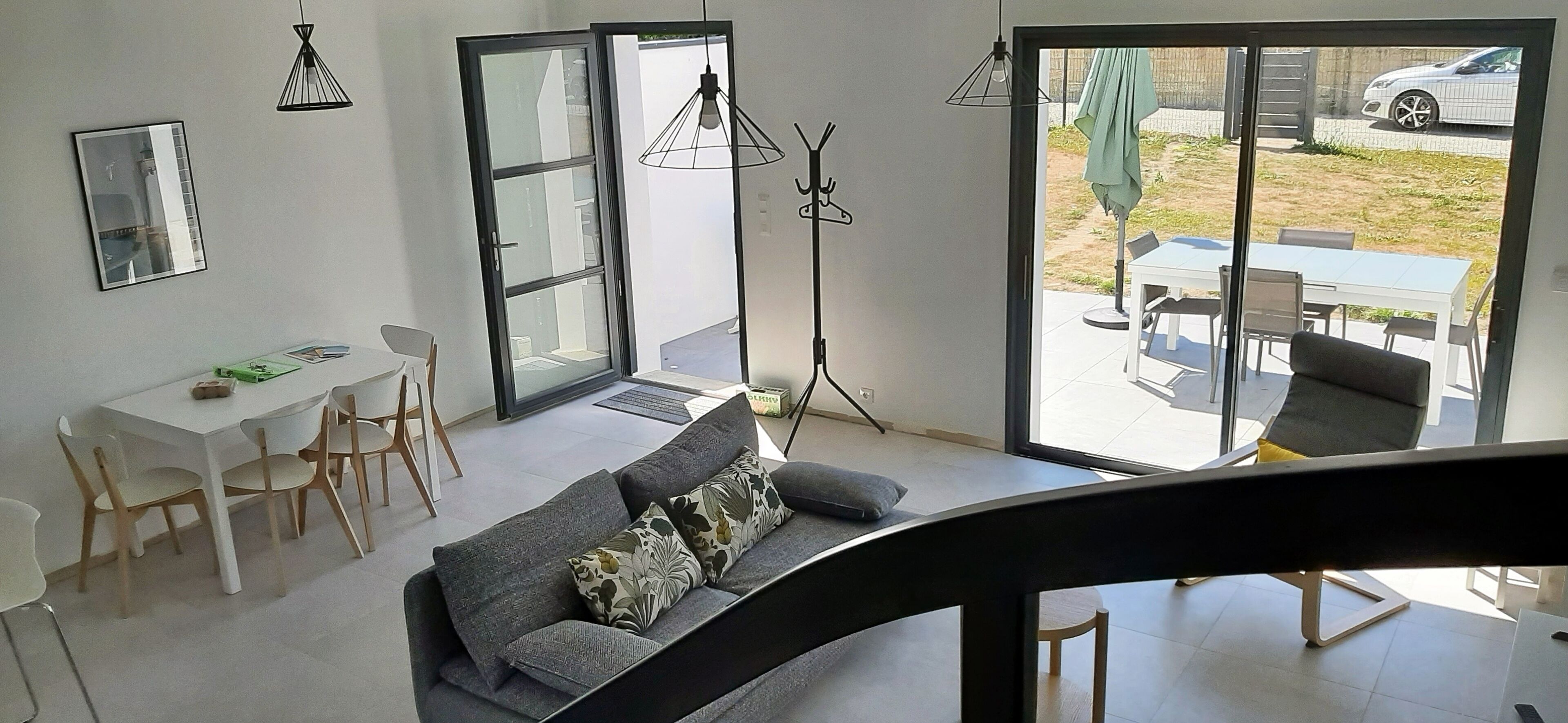 Un salon moderne comprenant un canapé, une table à manger et des chaises. Une grande porte-fenêtre coulissante donne accès à un espace extérieur aménagé avec une table et des chaises.