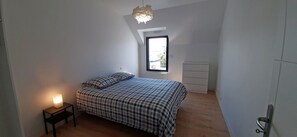 A bedroom with a bed, a bedside table with a lamp, a window with a view, and a wardrobe.