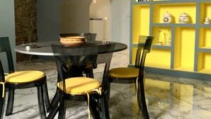 Comedor con una mesa redonda, cuatro sillas con cojines amarillos y un estante amarillo con libros y objetos decorativos.