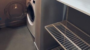 Un lavadero con lavadora, un estante con artículos de aseo y una unidad metálica de almacenamiento.
