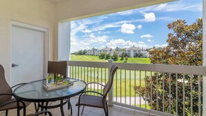 Ein Balkon mit Glastisch und Stühlen mit Blick auf einen Golfplatz und Gebäude.