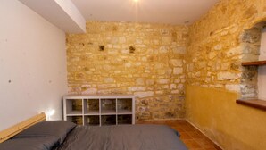 A bedroom with a stone wall, a bed with grey bedding, and a white bedside table. - Cozy house in Daglan with fireplace and terrace (Daglan)