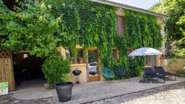 A building with a covered patio area featuring outdoor seating, a grill, and a large planter. - Cozy house in Daglan with fireplace and terrace (Daglan)