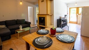 A dining area with a wooden table set for four, a fireplace, and a sofa in the background. - Cozy house in Daglan with fireplace and terrace (Daglan)