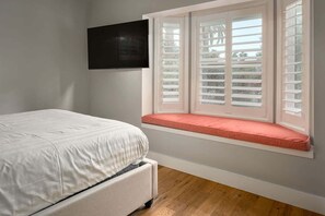 A bedroom with a bed, a window with shutters, and a television on the wall.