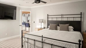 Ein Schlafzimmer mit einem Metallbettgestell, weißer Bettwäsche, einem Deckenventilator und einem Nachttisch mit Lampe.