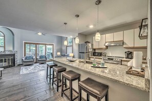 A modern kitchen with a large island, bar stools, and a dining area with a fireplace. - Dreamy, Family-Friendly Cloudcroft Townhome! (Cloudcroft)