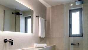 Un baño moderno con un espejo grande, un lavamanos blanco y una ducha con mampara de vidrio.