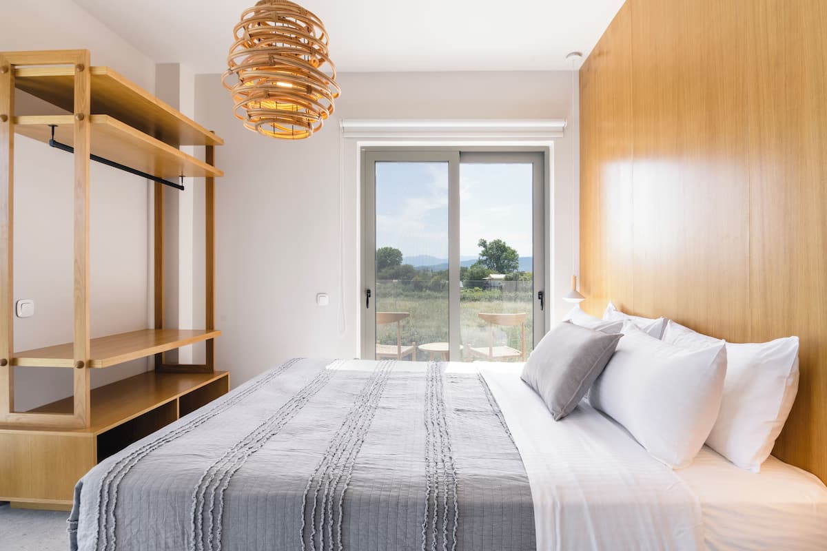 Un dormitorio con cama, un armario de madera y vistas a través de un ventanal.