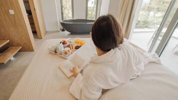 A person reading a book on a bed with a tray of breakfast items and a bathtub in the background.