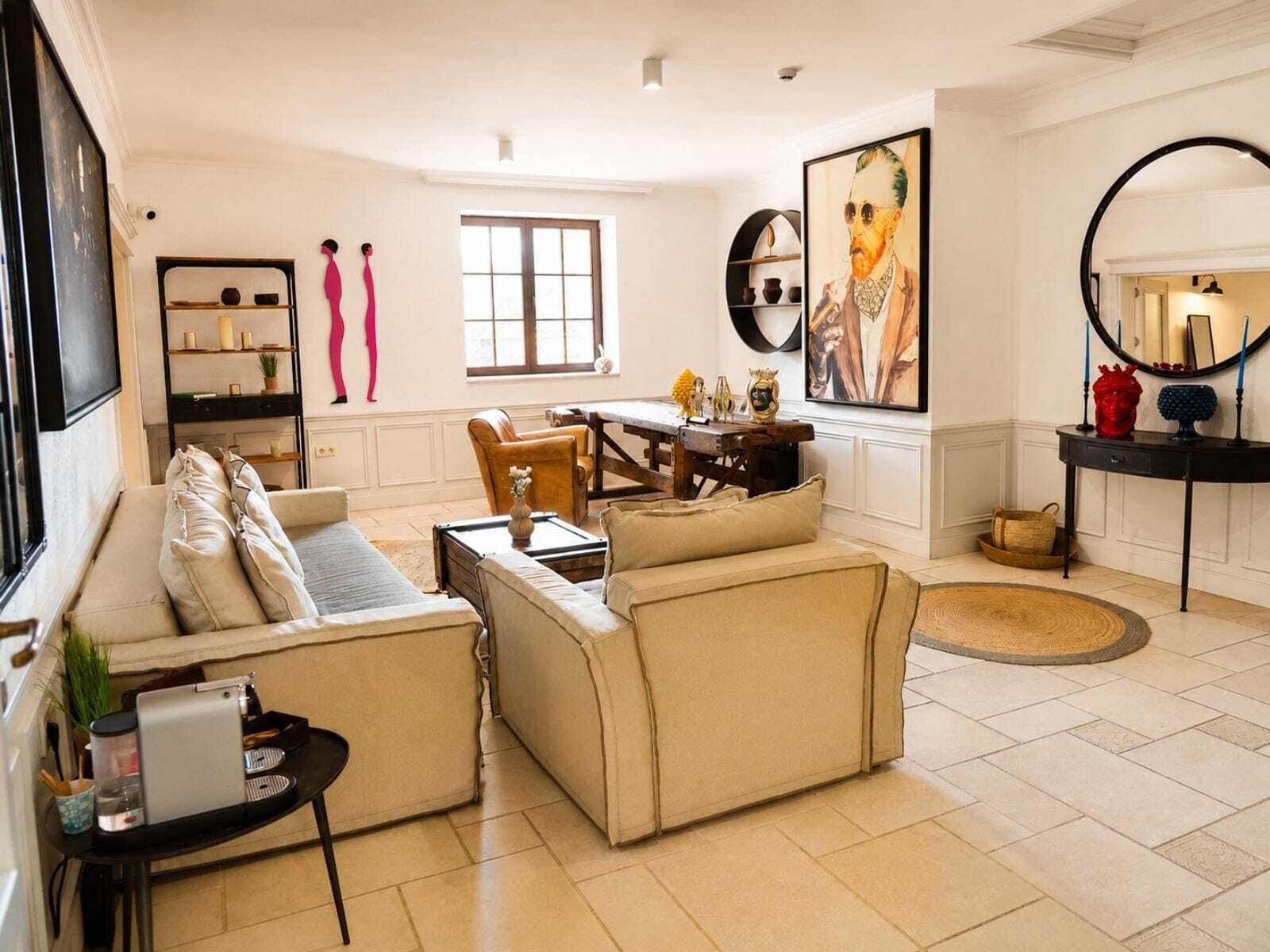 A living room with a sofa set, a dining table, and a coffee table. There is a window, a painting on the wall, and a mirror.