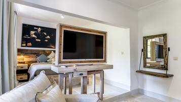 A modern living room with a large flat-screen TV, a wooden coffee table, a sofa, and a large mirror on the wall.