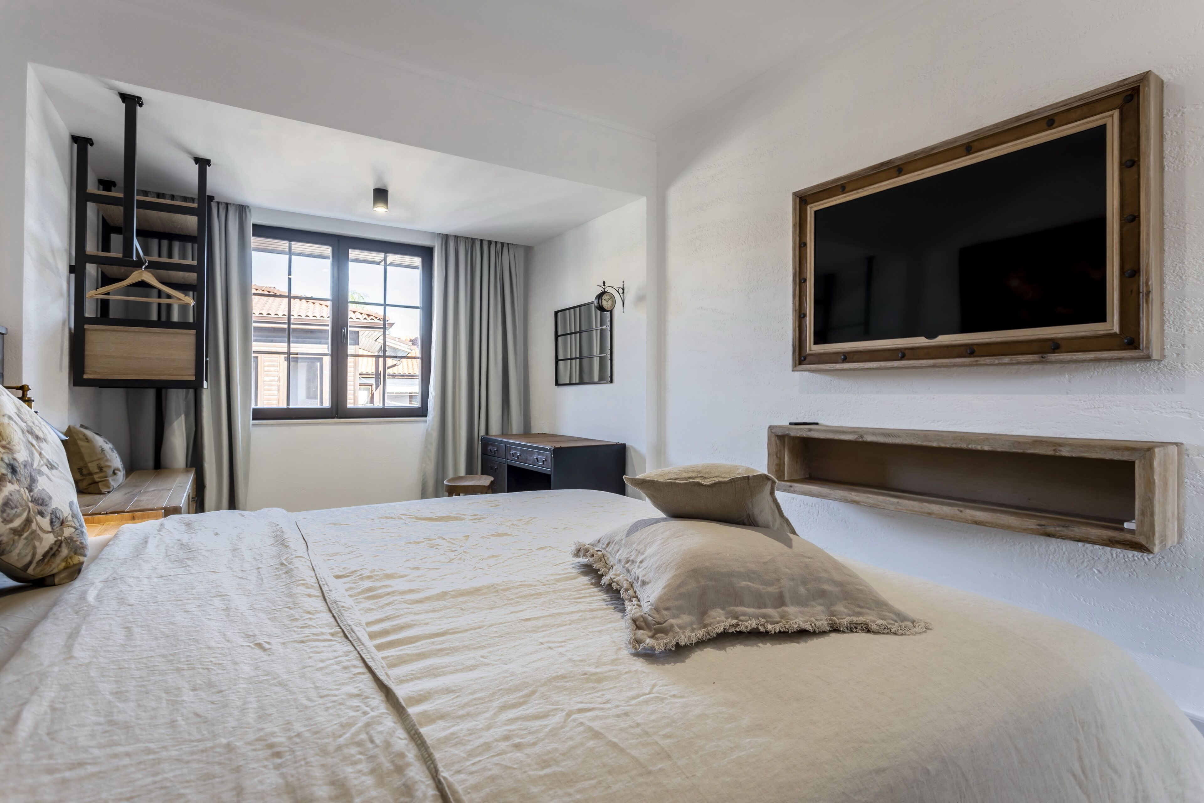 A bedroom with a large bed, a wardrobe, a desk, and a window with curtains.