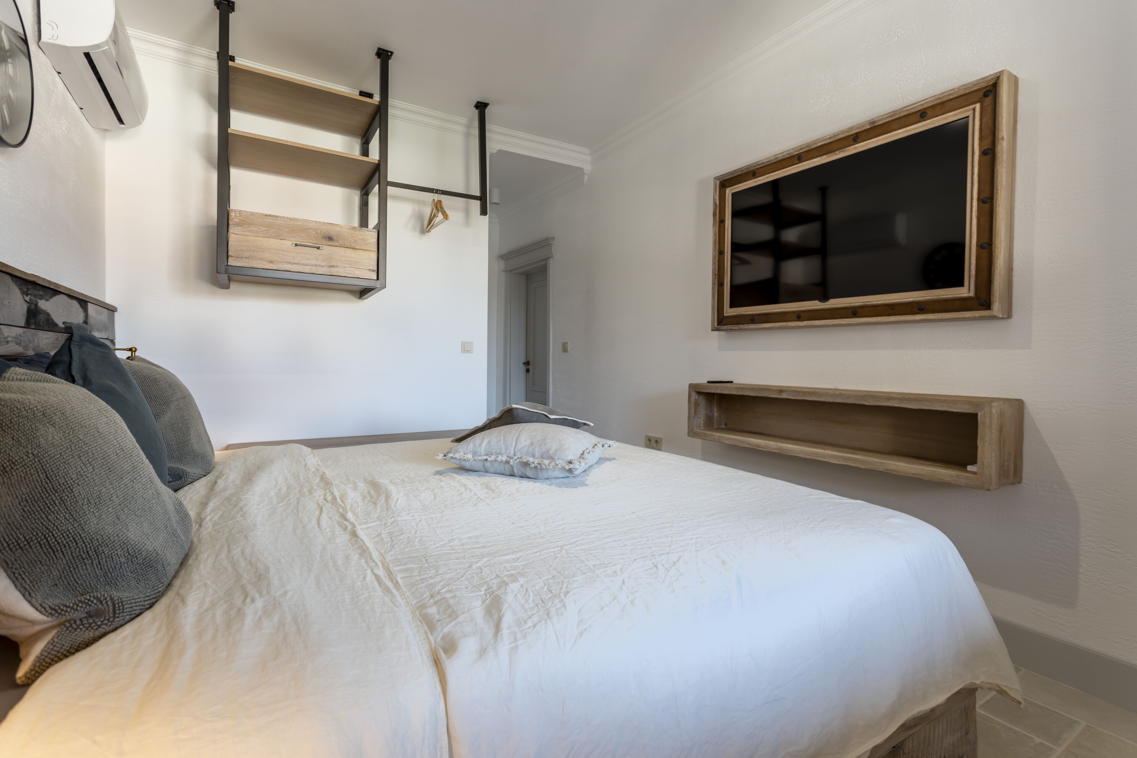 A bedroom with a bed, pillows, a wooden shelf, and a mirror.