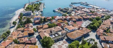 An aerial view of a coastal town with a marina, historic buildings, and a central square with circular patterns.