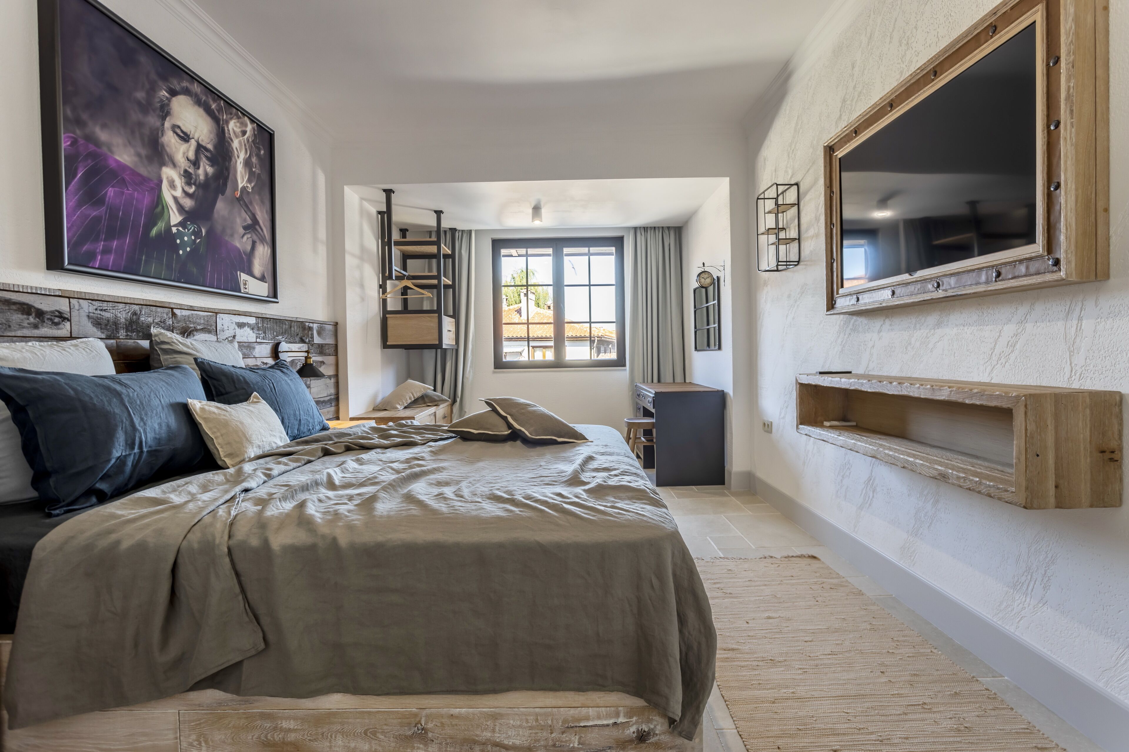 A bedroom with a large bed, a painting, a window, and a mirror.