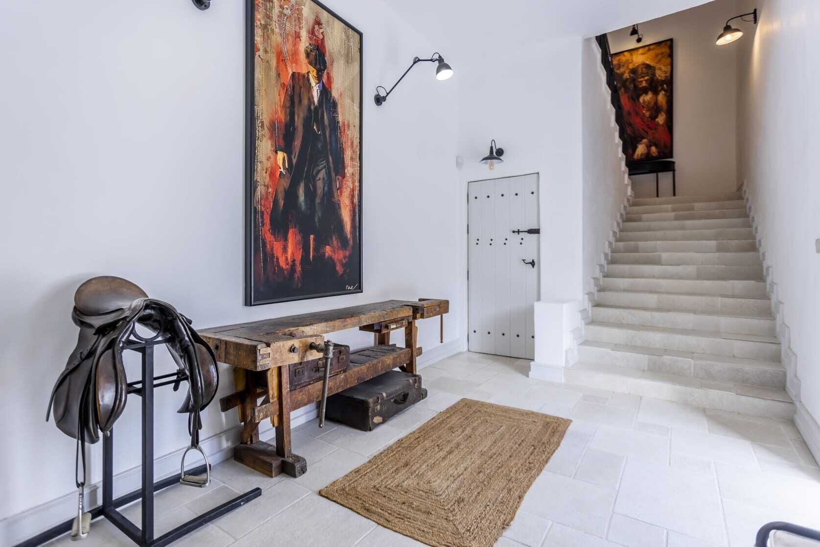 Ein modernes Interieur mit Treppe, einem aufgehängten Gemälde, einer Holzbank und einem Sattel.