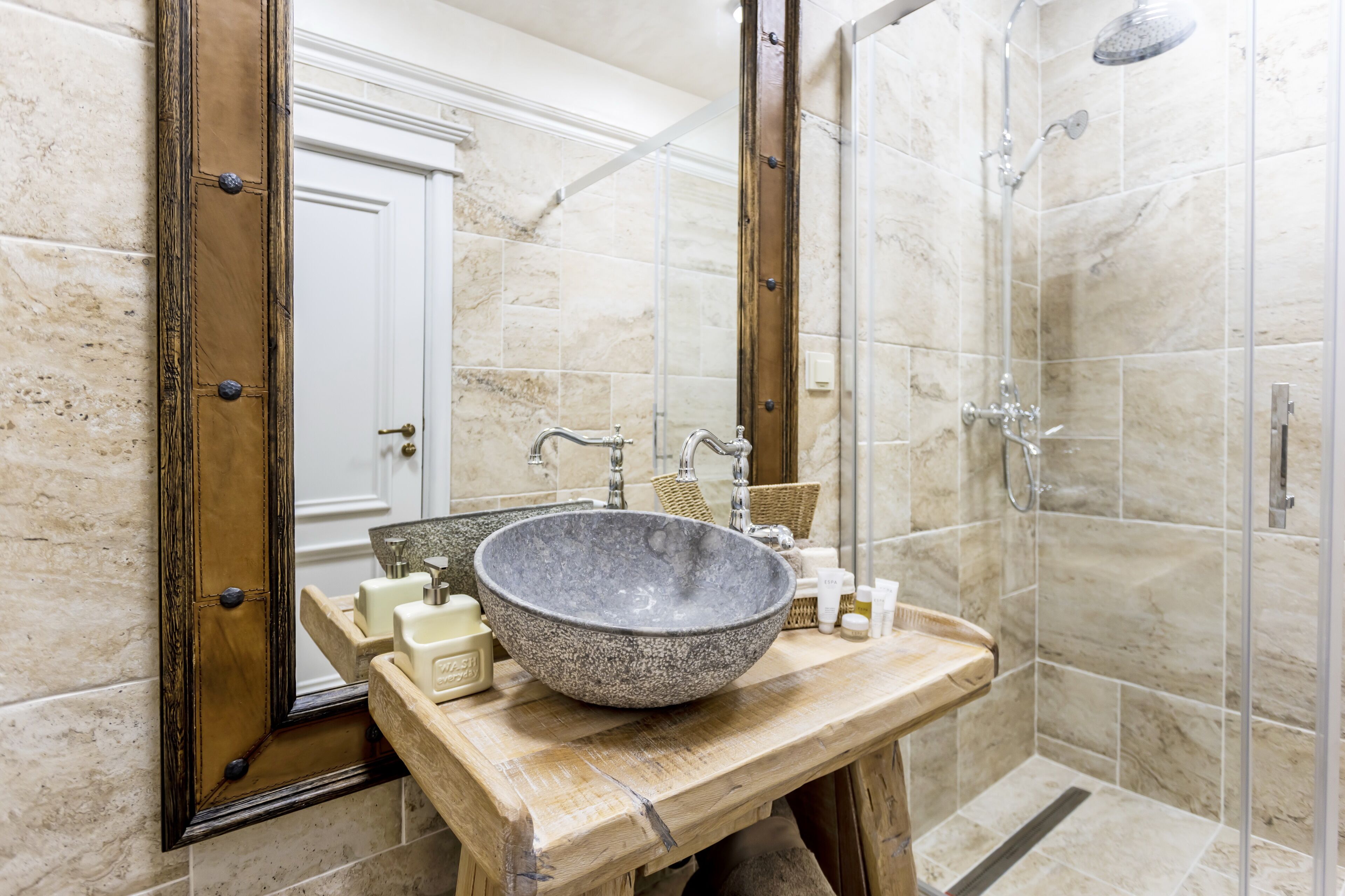 A bathroom with a large stone sink, a wooden vanity, a mirror, and a shower area.
