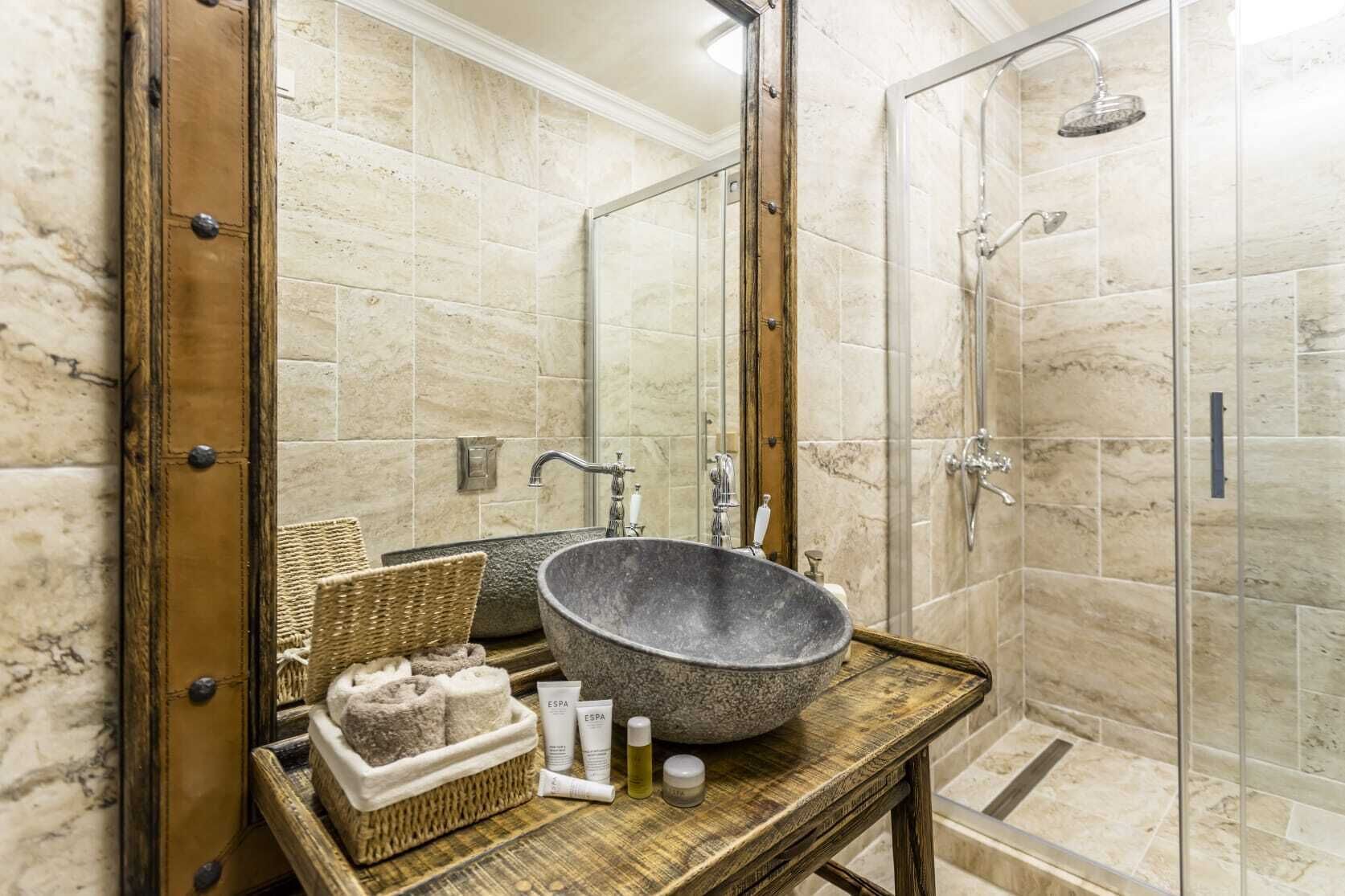 A bathroom with a large stone sink, a wooden vanity, a glass shower enclosure, and a mirror with a wooden frame.